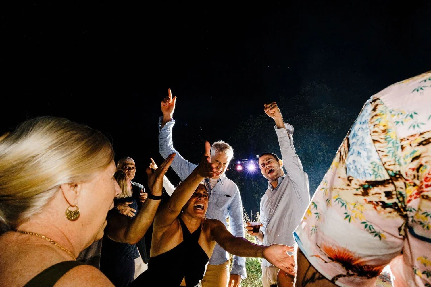 A lively group of people dance and cheer at a nighttime celebration.