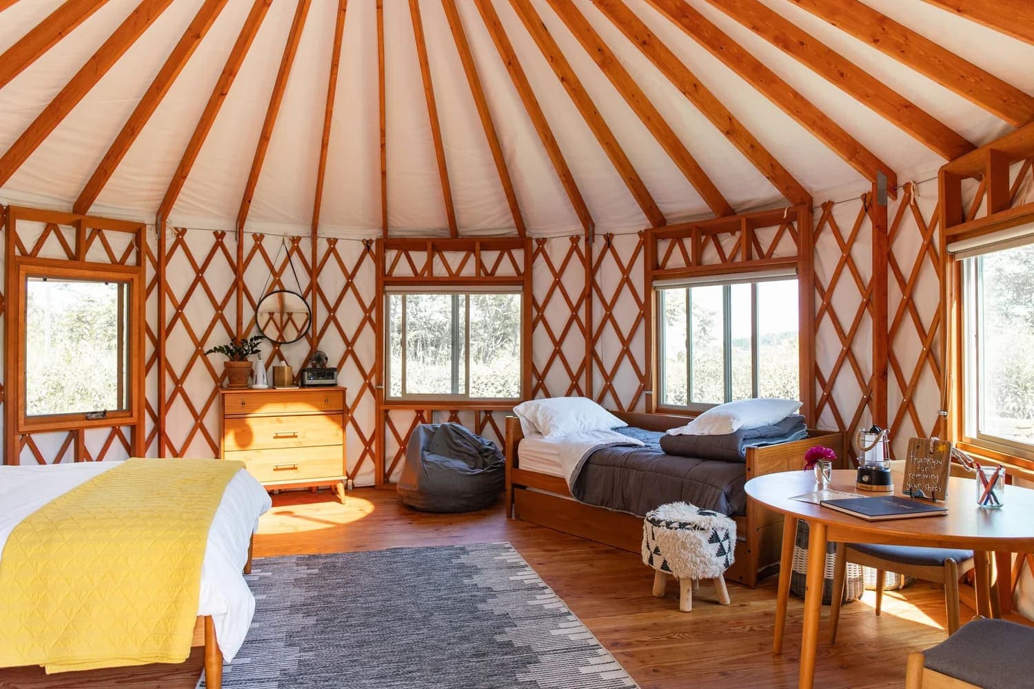 Interior of a cozy yurt featuring two beds, a wooden table, and large windows.