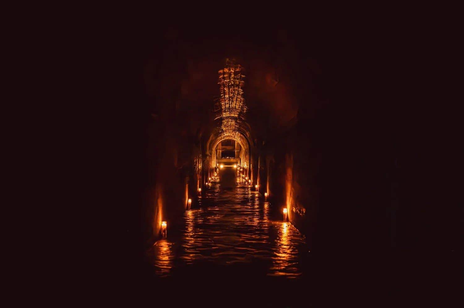 A dimly lit tunnel with flickering lights reflecting off water.