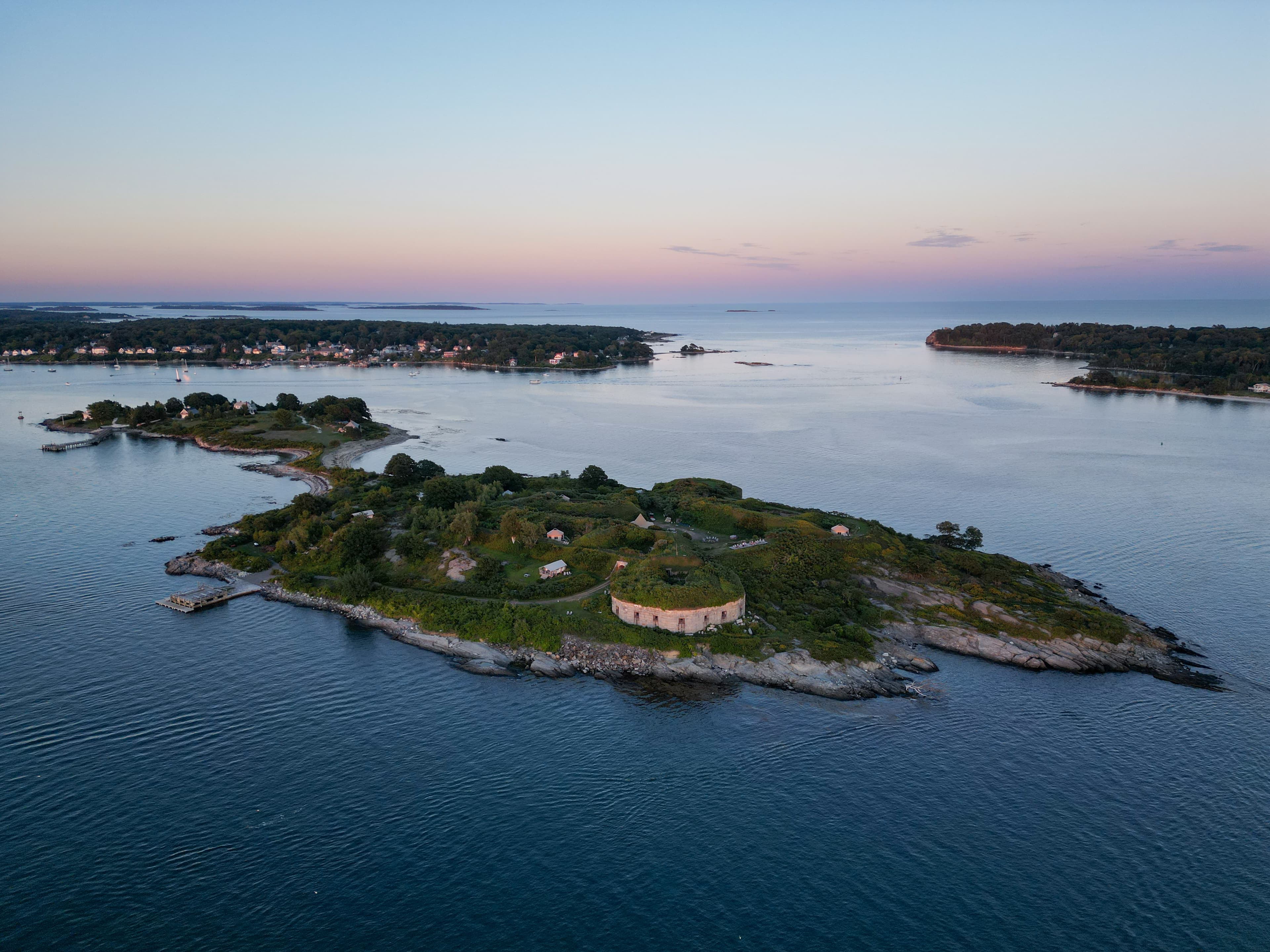 Aerial view of a small island surrounded by calm waters at sunset.