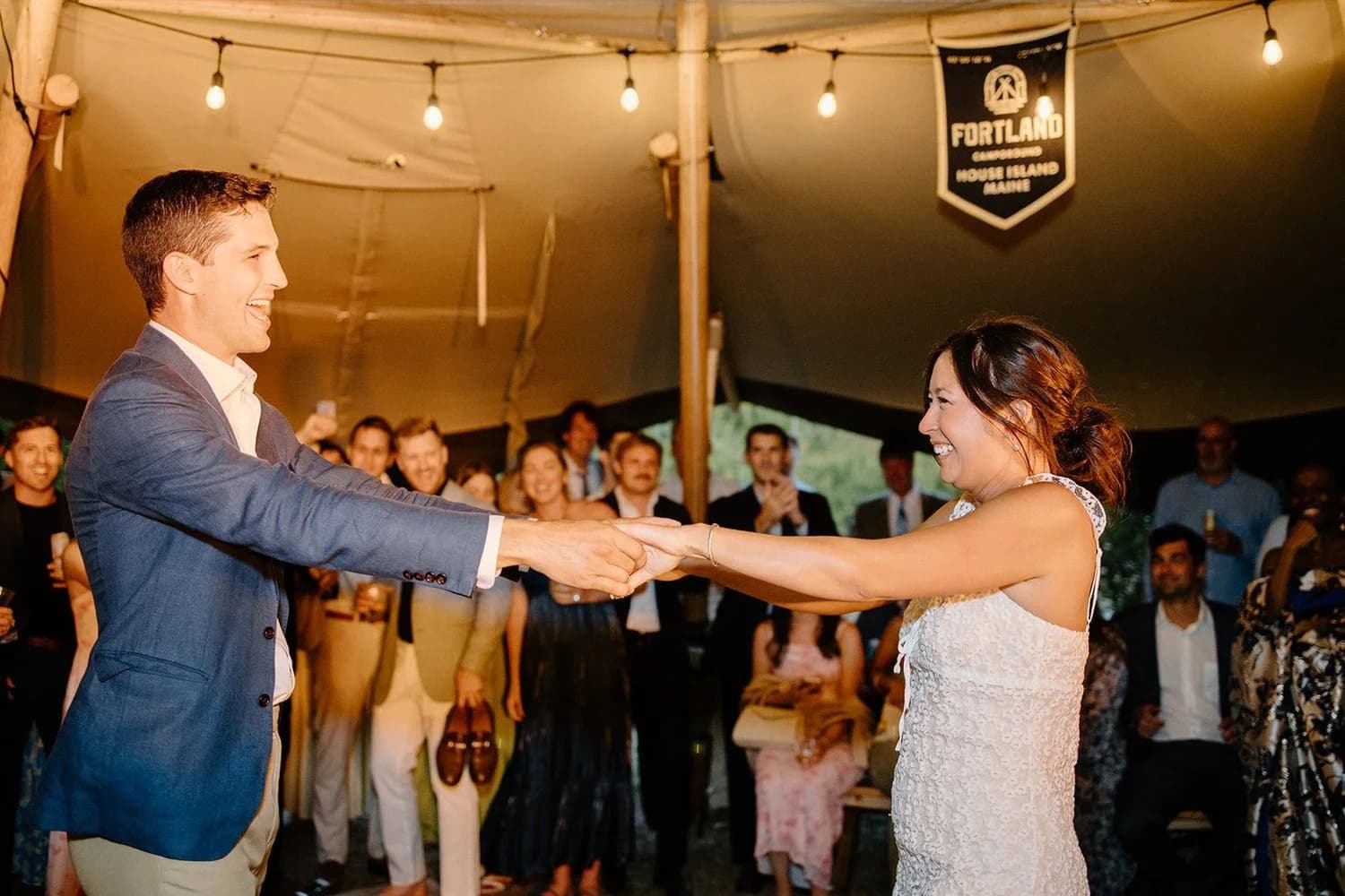 A couple shares a joyful moment while dancing at a wedding reception in a tent.