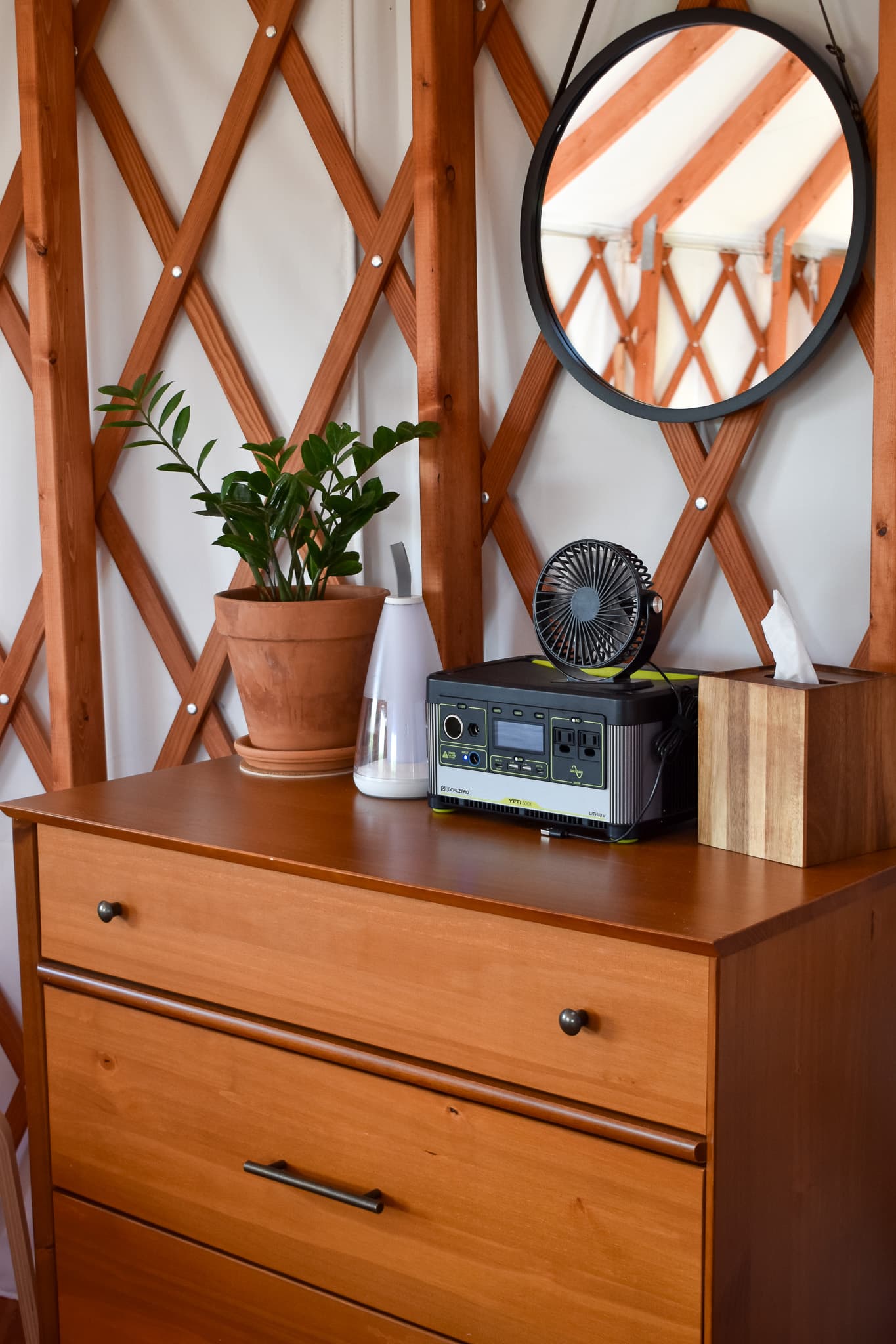 A wooden dresser with a plant, a fan, and various small items set against a backdrop of wood paneling.