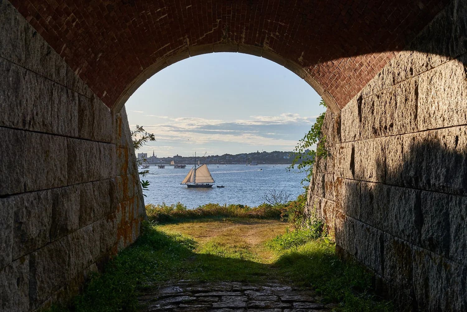 View of a sailboat on the water framed by an arched stone passageway.