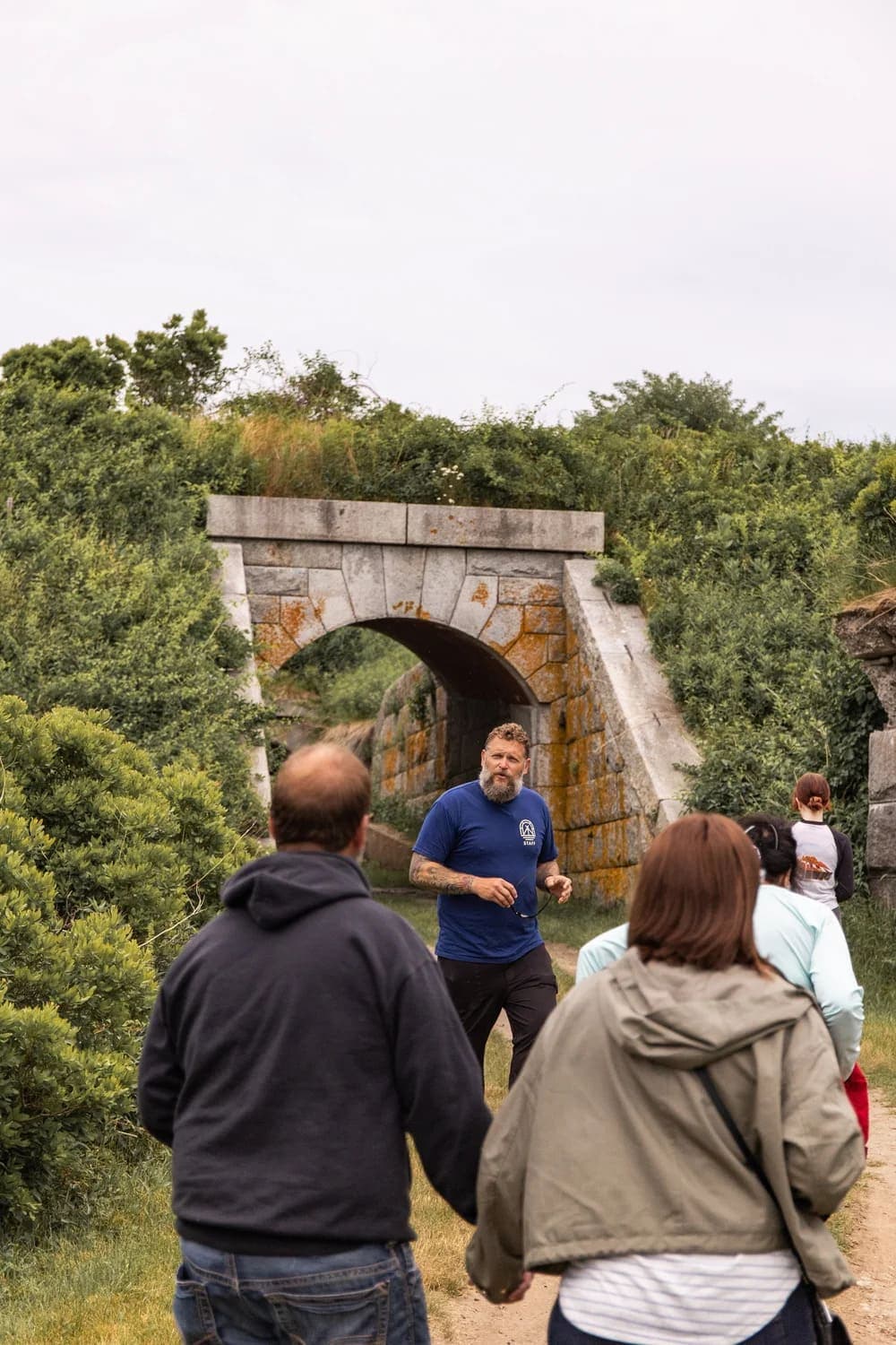A group of people walks towards a stone archway in a green landscape.