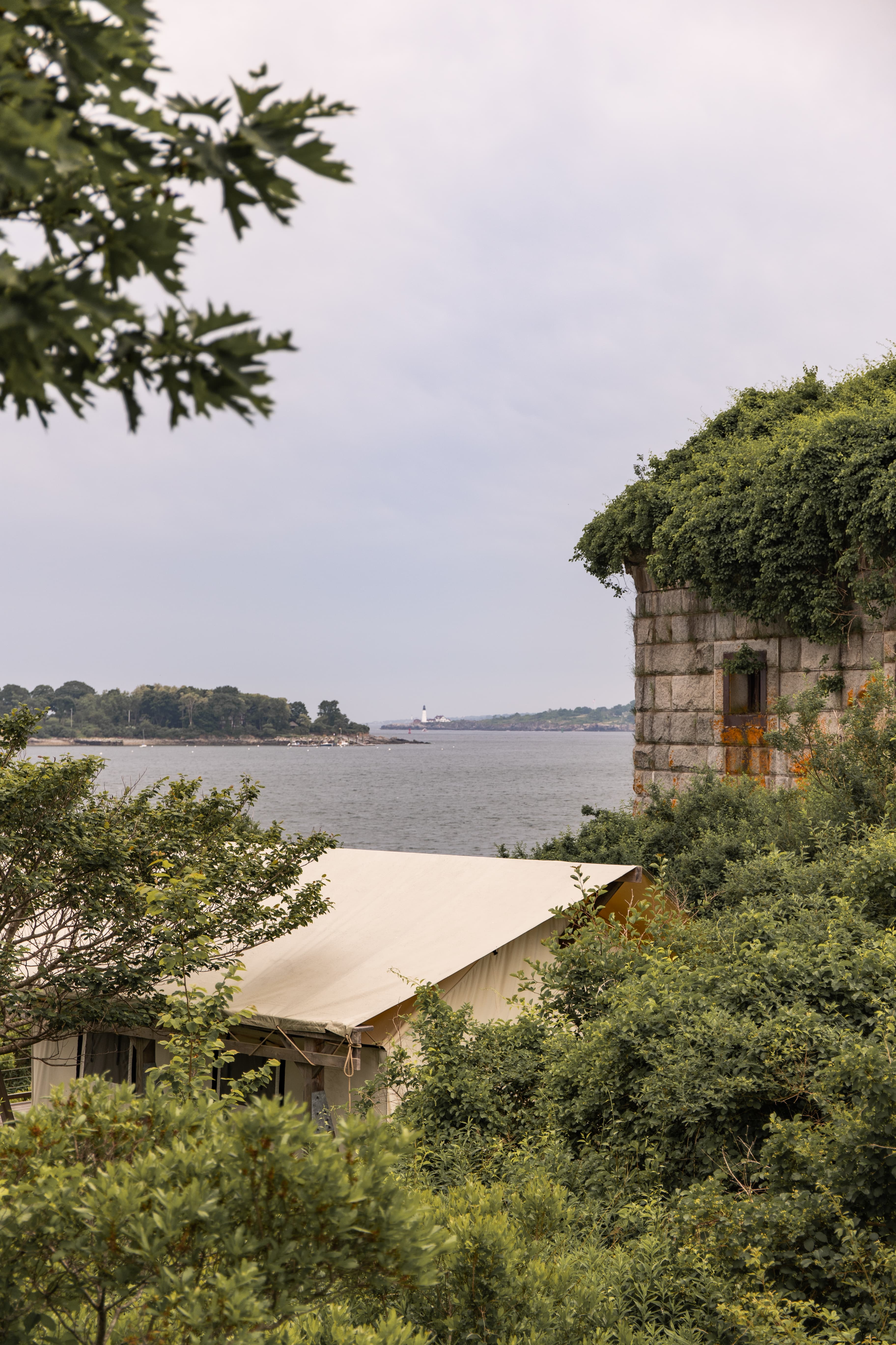 A coastal view featuring a stone structure covered in vegetation, with a tent and the sea in the background.