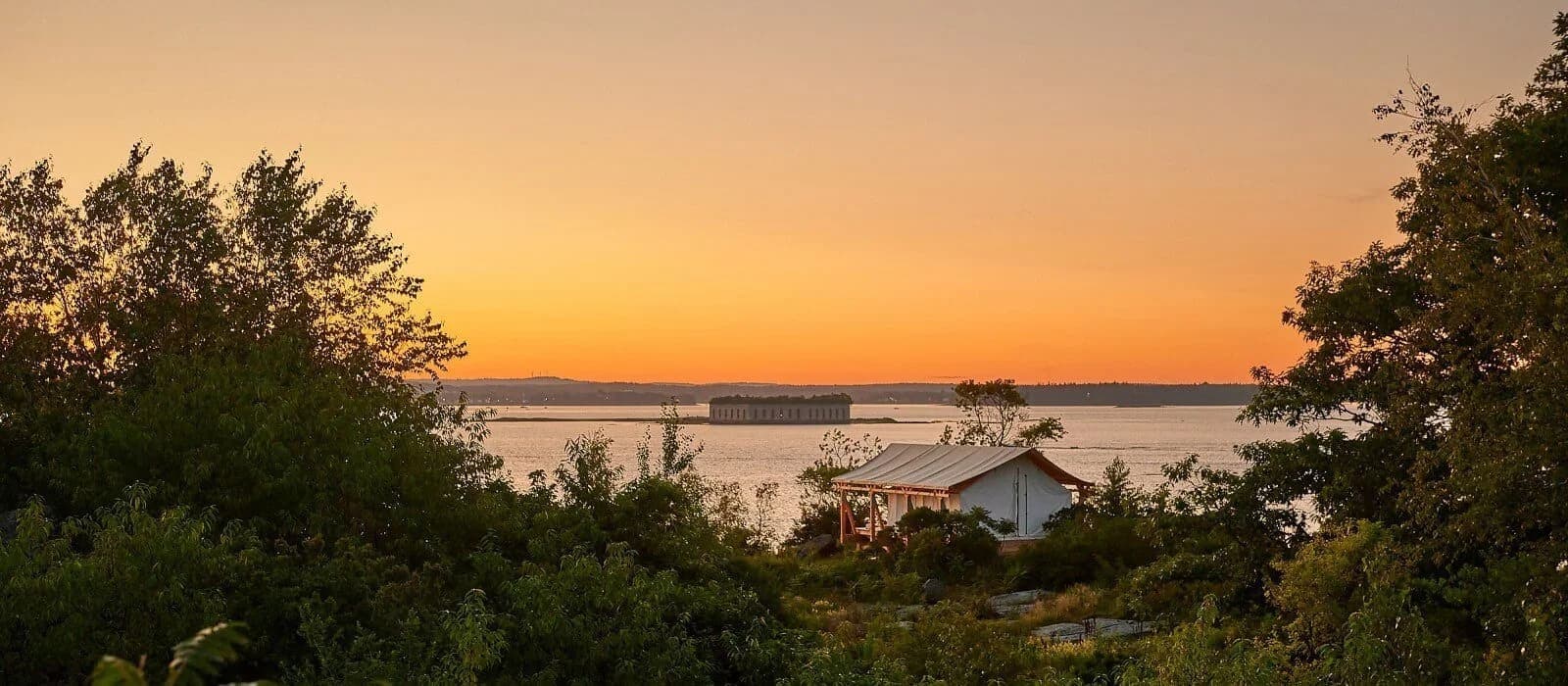Serene sunset over a calm lake with a house and trees in the foreground.
