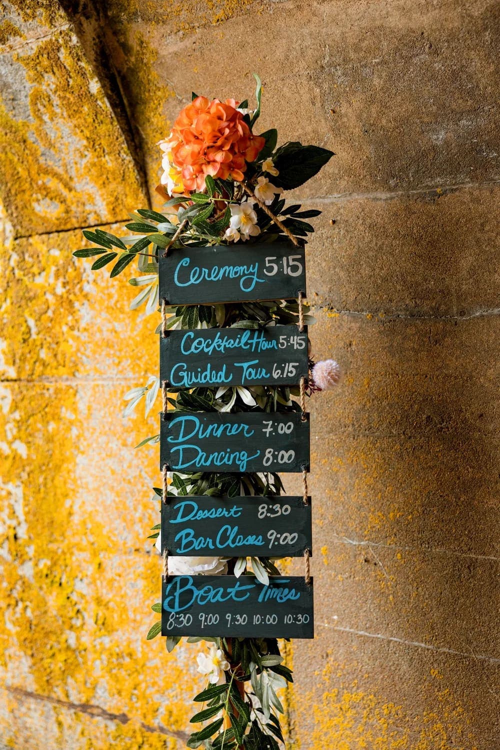 A decorative schedule board displaying event timings, including ceremony, dinner, and boat times, adorned with flowers.