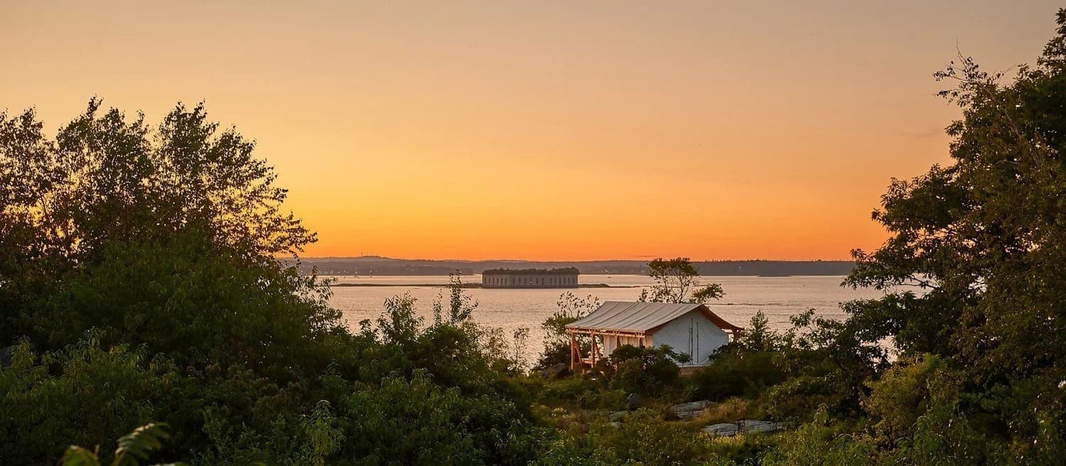 A serene sunset over a coastal landscape featuring a white house and distant ships.