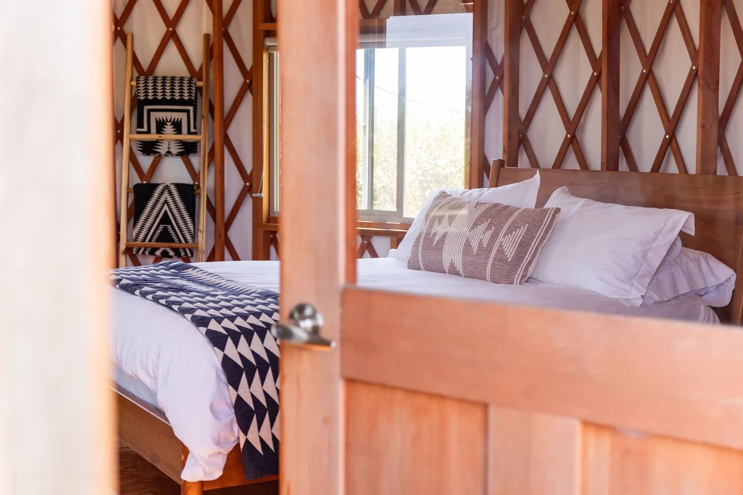 A cozy bedroom featuring a wooden bed, decorative pillows, and geometric-patterned textiles, seen through an open door.