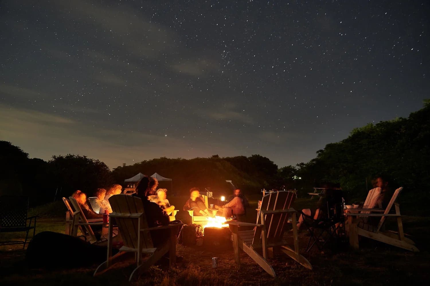 A group of people gathers around a campfire under a starry night sky.