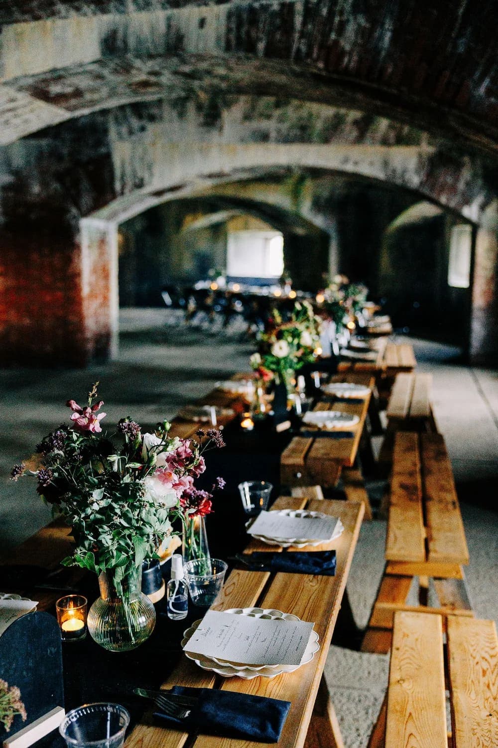 A long table setting with floral arrangements and place settings in a rustic venue.