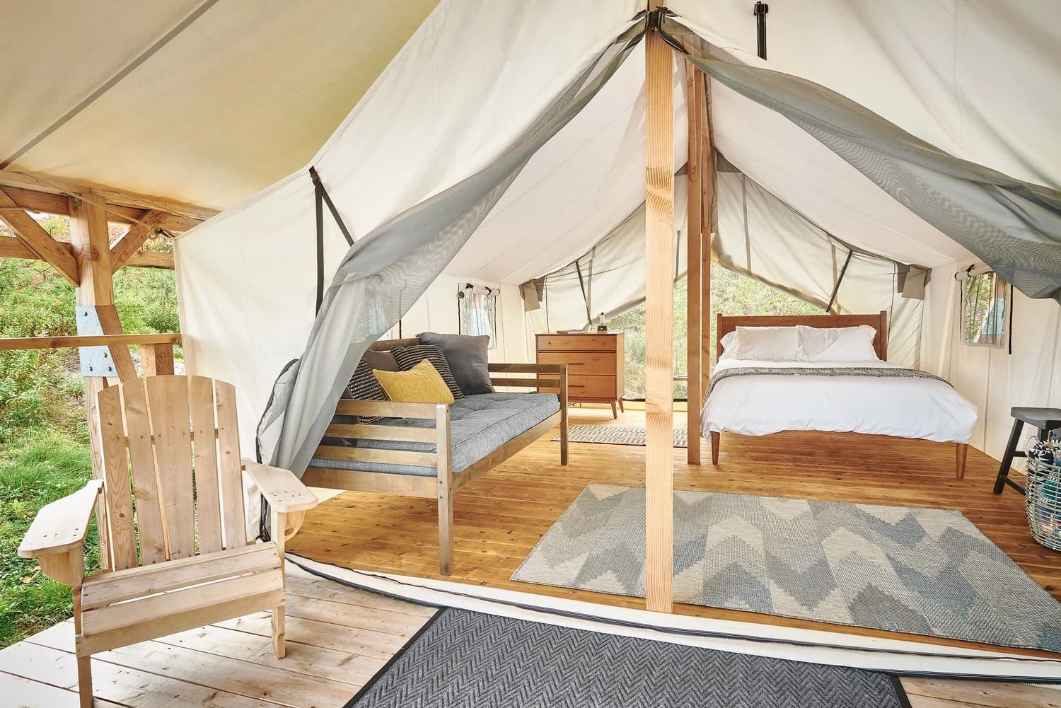 Cozy glamping tent interior featuring a bed, seating area, and wooden furnishings.