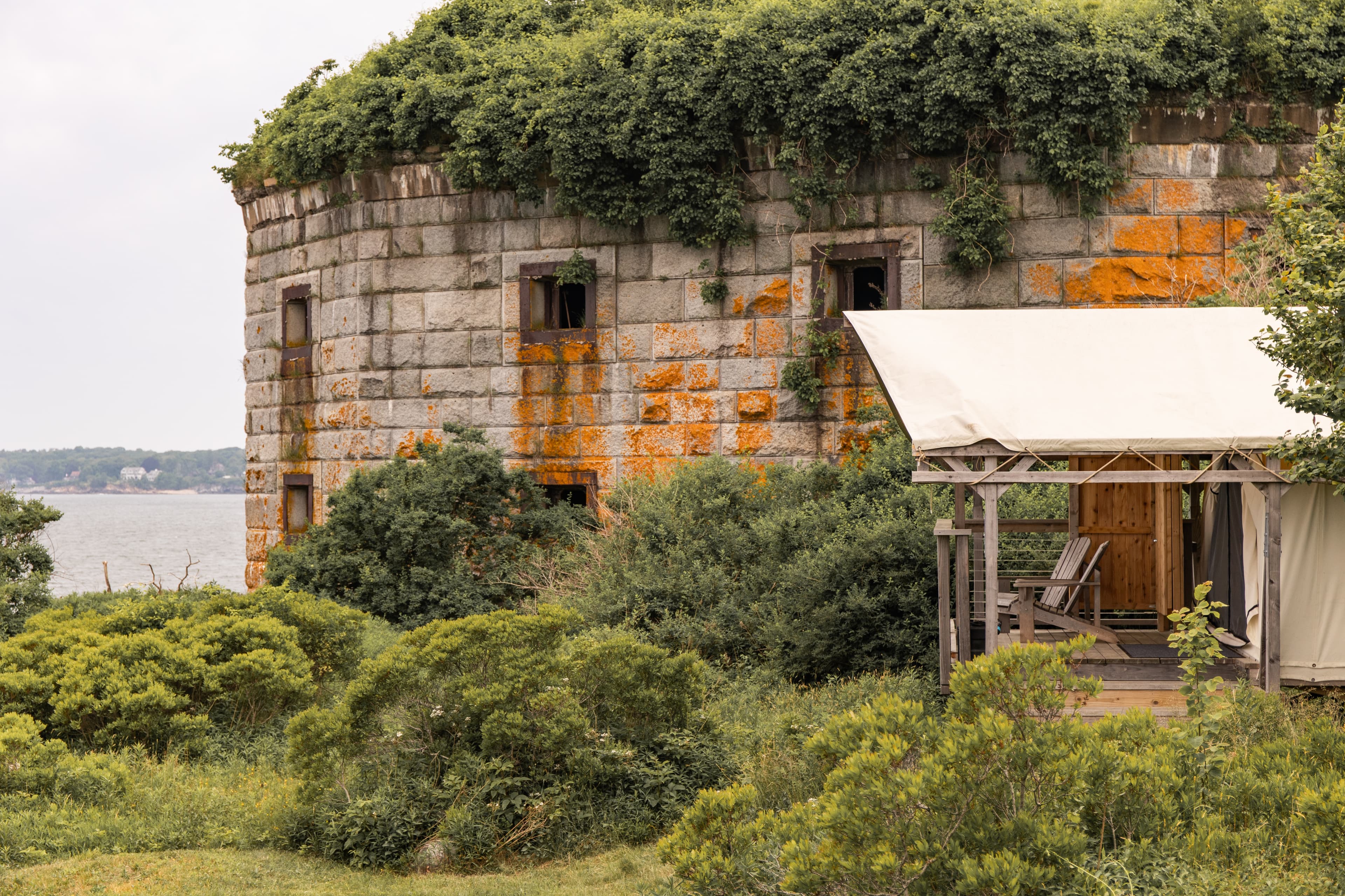 Abandoned stone fort covered in greenery near a body of water.
