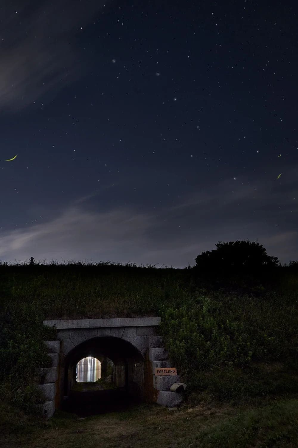 A stone tunnel under a starry night sky leads to a distant, illuminated opening.