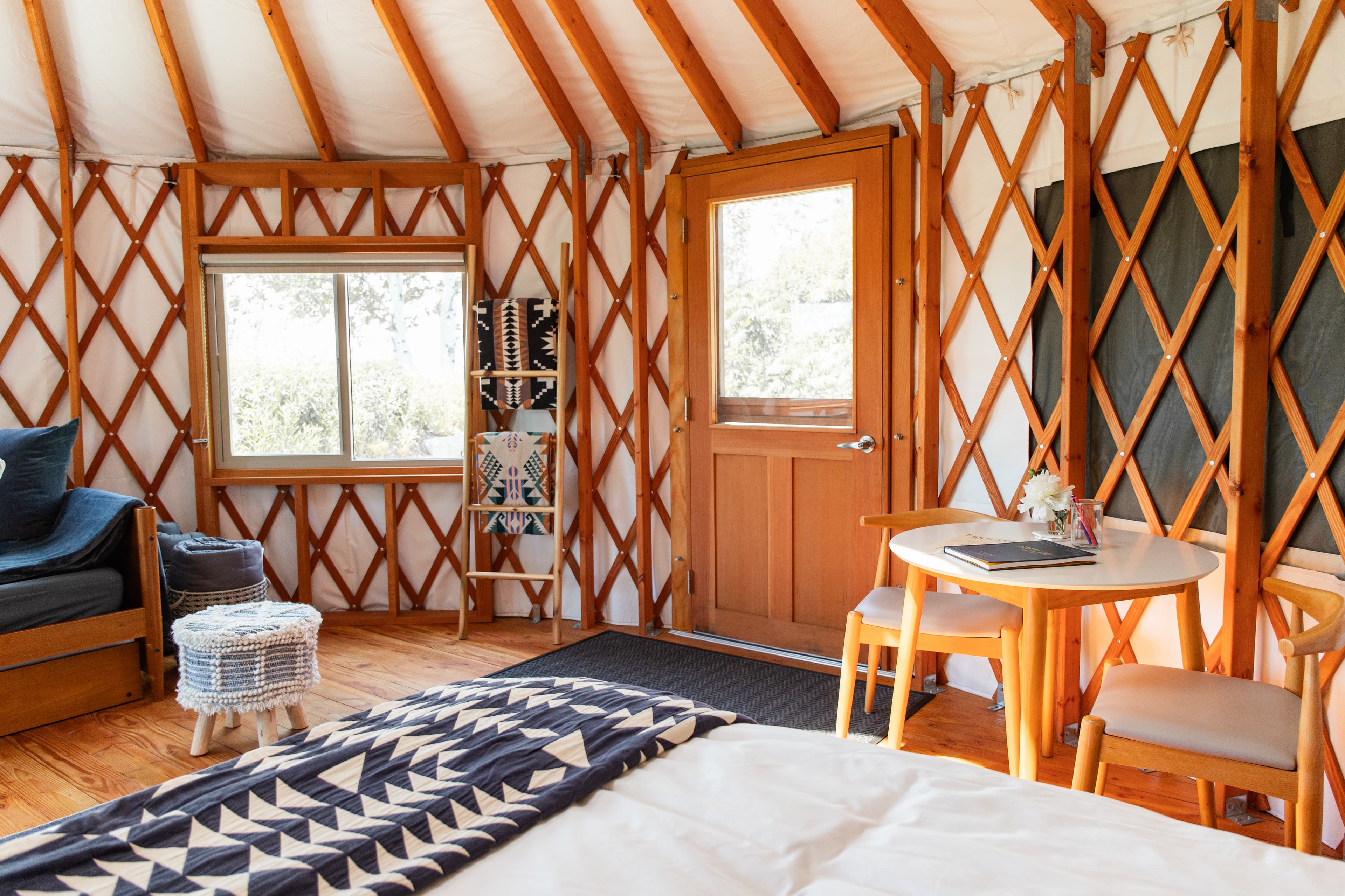 Interior of a cozy yurt featuring wooden beams, a bed, seating area, and a door leading outside.