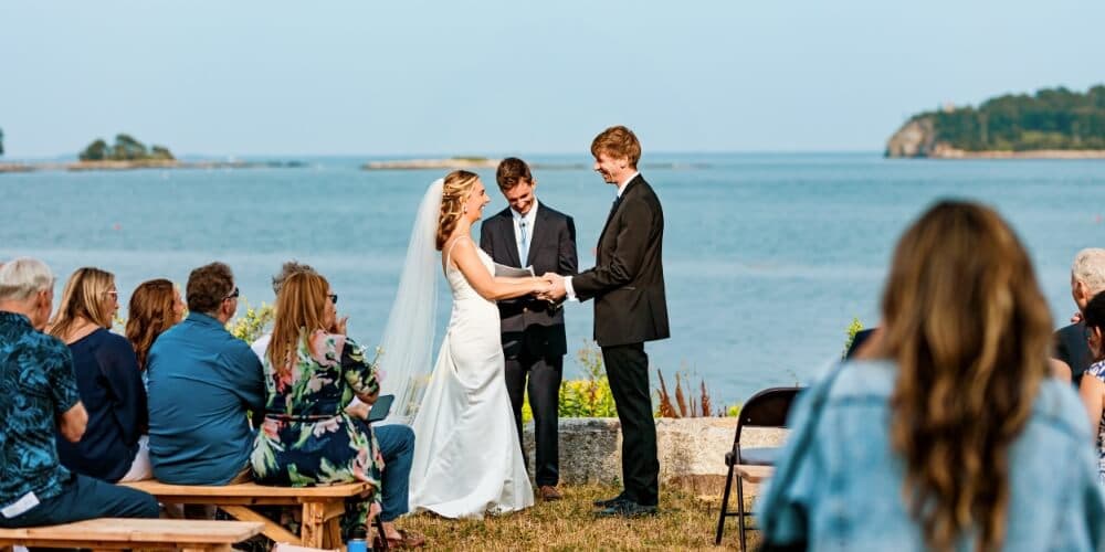 A bride and groom exchange vows during an outdoor wedding ceremony by the sea.