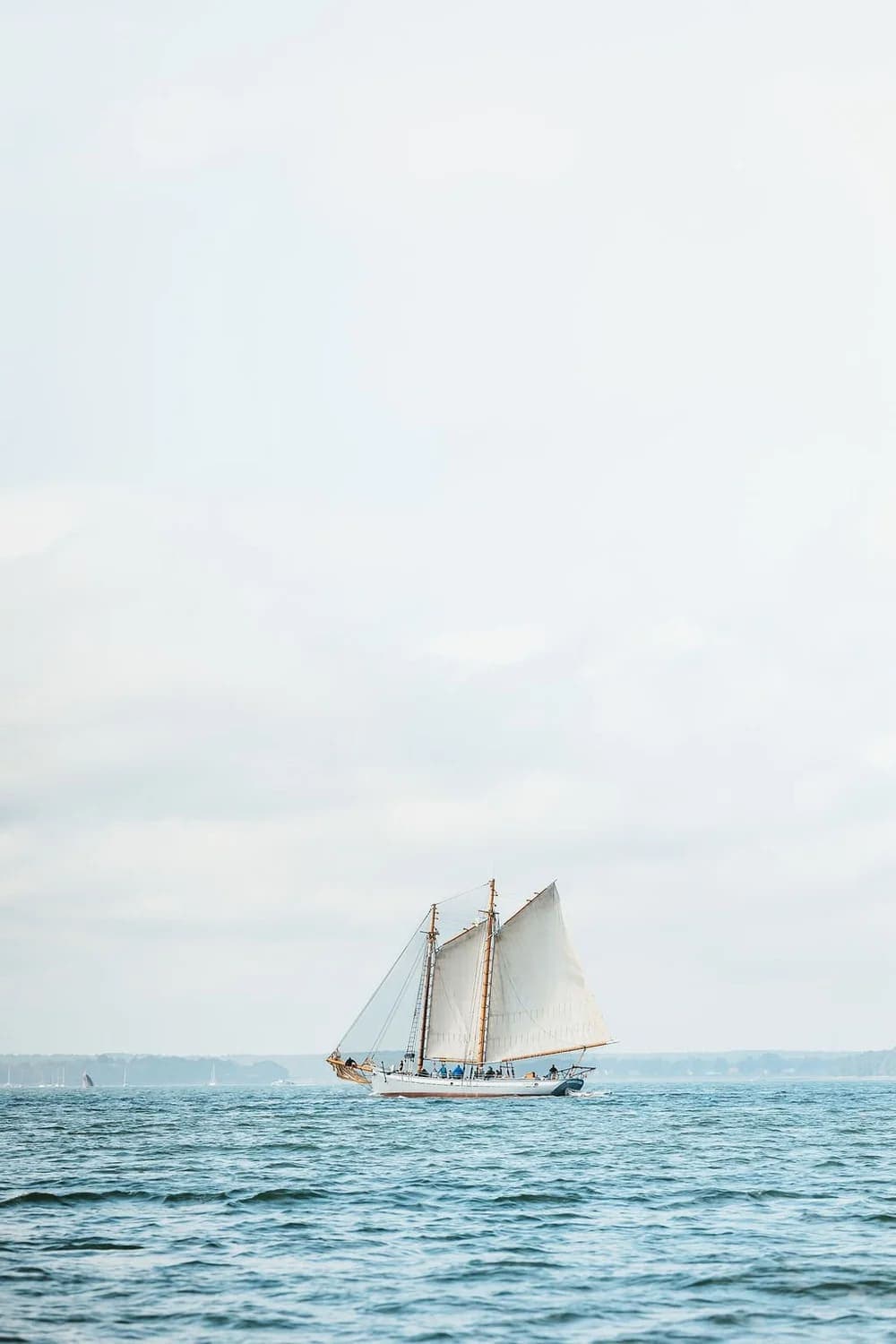 A sailboat glides across calm waters under a light gray sky.