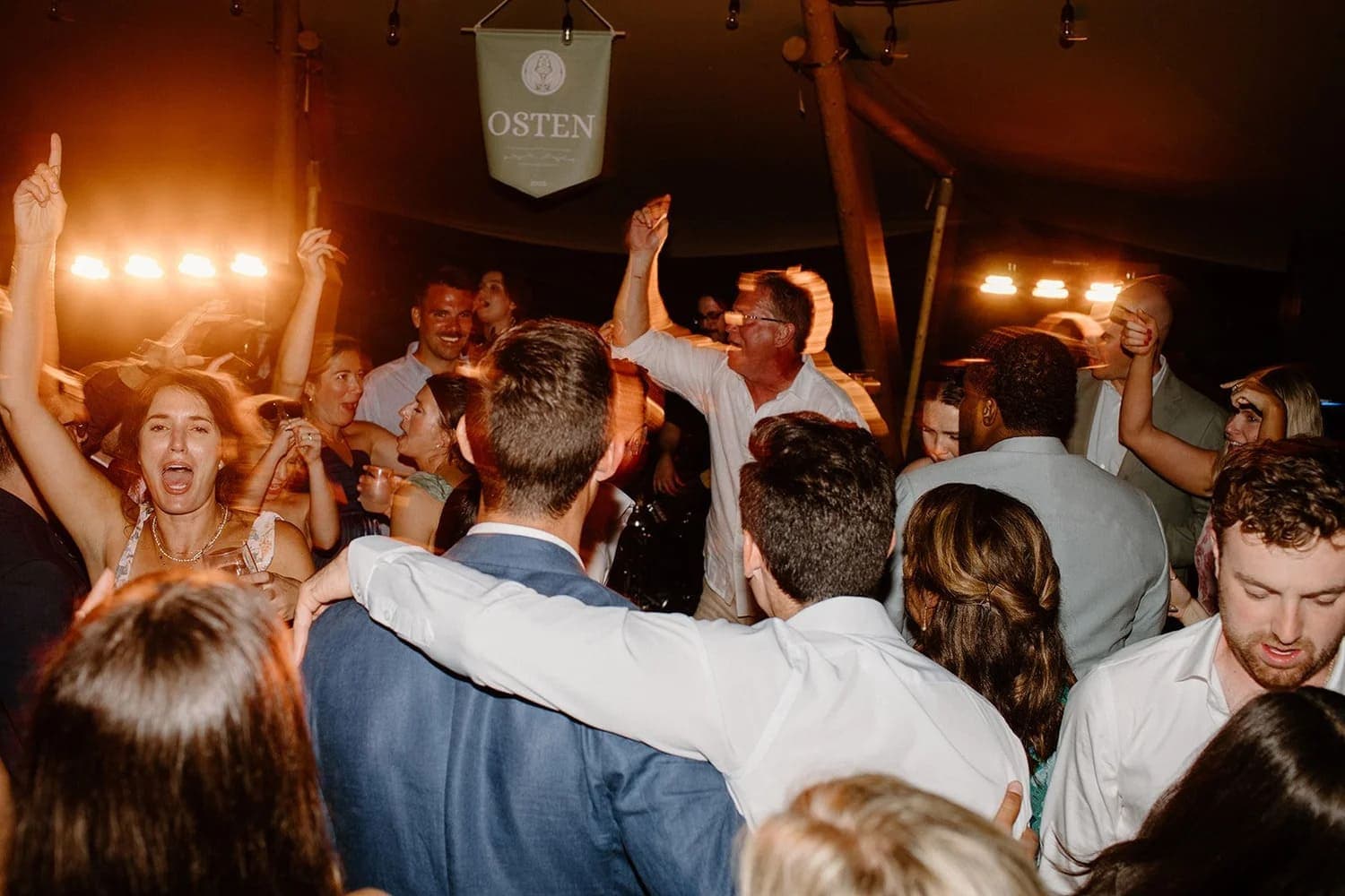 A lively crowd dances and celebrates under warm lighting at an event.