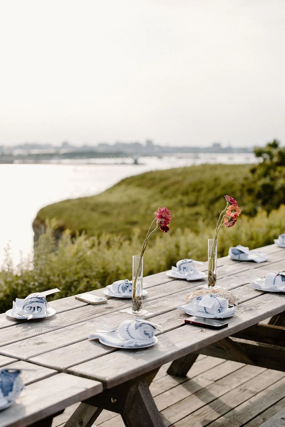 A beautifully set outdoor dining table with flowers and tableware overlooking a serene landscape.