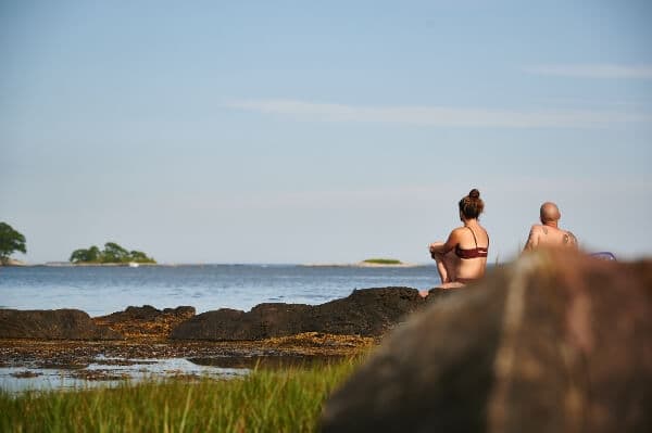 2 people sitting on some boulders overlooking the ocean