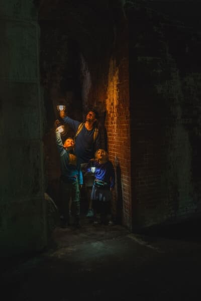 a family walking through undergound tunnels at a fort, lit only by the lanterns in their hands