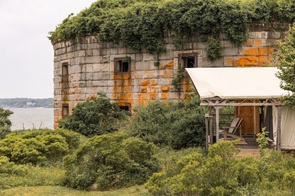 An old fort building with a glamping tent next to it, overlooking the ocean